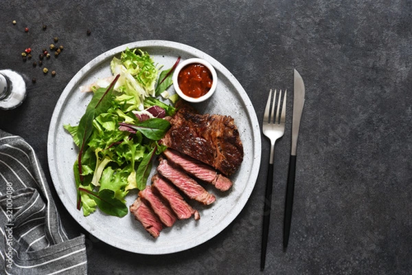 Fototapeta Grilled marbled beef steak with salad in a plate on the kitchen table. With copy space under the text.