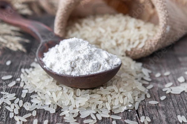 Obraz Rice flour in a spoon on a pile of white rice on old boards.