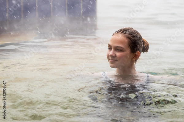 Obraz Girl in the pool with warm mineral water from a thermal spring in winter in snowy weather outdoors. Steam rises from warm water.