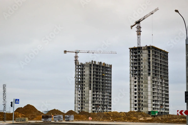 Fototapeta Construction of a new microdistrict with high houses, new buildings with developed infrastructure with the help of large industrial cranes and professional construction equipment in a big city