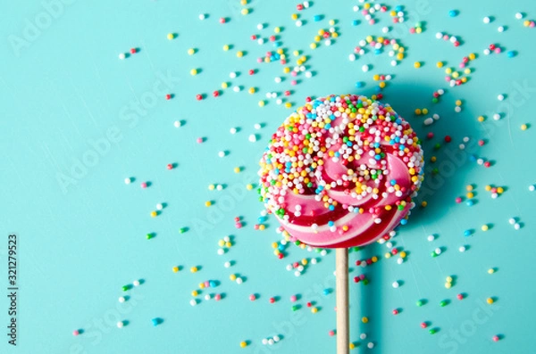 Fototapeta Colorful lollypop candy with red stripes and sprinkles on blue mint background for holidays