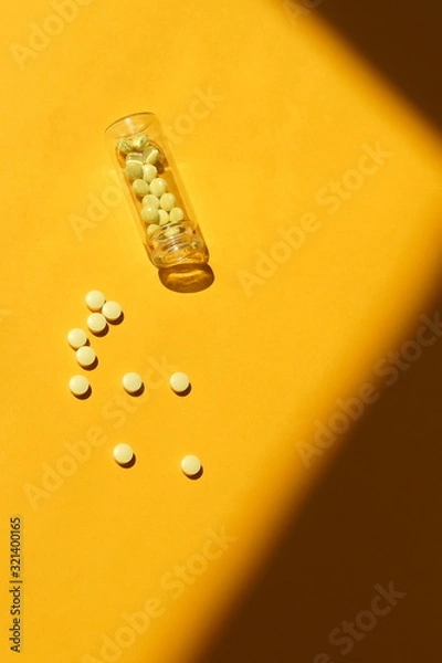 Fototapeta Yellow pills in a bottle on yellow  background with sun shadows. top view, copy space