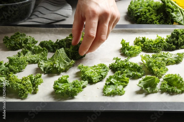 Fototapeta Woman preparing kale chips at table, closeup