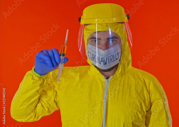 Obraz Man in yellow chemical protection suit and face protective mask coronavirus. Without glasses. Protective helmet. Hands in blue gloves. Yellow vaccine syringe.