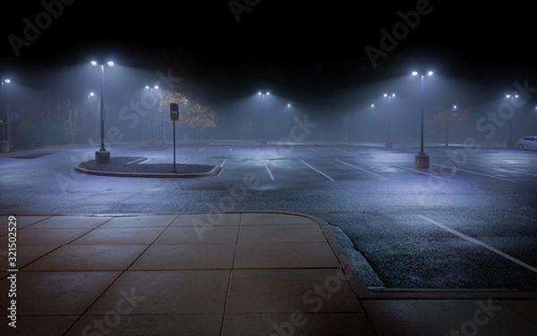 Fototapeta An Empty Parking Lot on a Cold, Rainy Night - with Vacant Parking Spaces and a Thick Mist Gathering Under the Lights