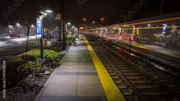 Fototapeta An Empty Light Rail Station in Baltimore Maryland on a Cold, Rainy Night - with Light Streaks from a Passing Train and a Thick Mist Gathering Under the Lights