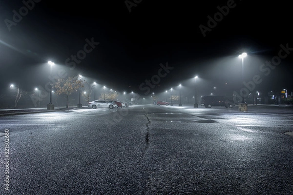 Fototapeta A Lonely Parking Lot on a Cold, Rainy Night - with a Small Collection of Parked Cars in the Background and a Thick Mist Gathering Under the Lights