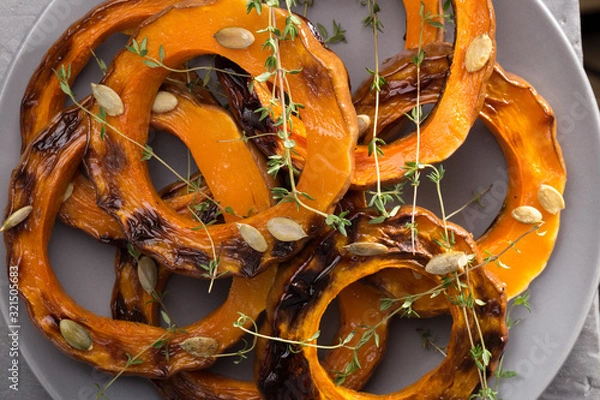 Obraz Pumpkin grill served on a plate. Baked pumpkin sliced rings with a knife, fork and napkin on a concrete table. Autumn dish. Halloween dish. Everyday autumn kitchen. Orange colors. space for text.  