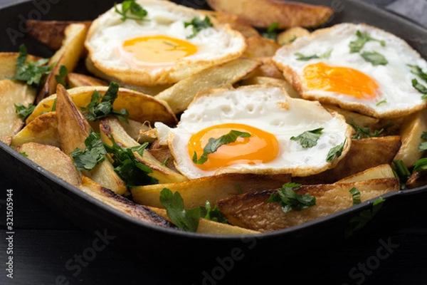 Obraz Breakfast in the pan. Fried potatoes with eggs in a skillet. Food bachelor. Cooked by a man. Hot and fresh. Homemade breakfast on black table. Fried eggs and sweet potato hash in cast iron skillet Fre