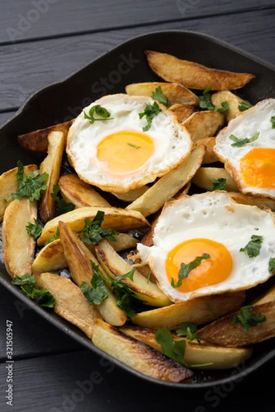 Obraz Breakfast in the pan. Fried potatoes with eggs in a skillet. Food bachelor. Cooked by a man. Hot and fresh. Homemade breakfast on black table. Fried eggs and sweet potato hash in cast iron skillet Fre