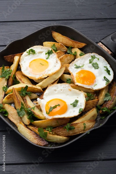 Obraz Breakfast in the pan. Fried potatoes with eggs in a skillet. Food bachelor. Cooked by a man. Hot and fresh. Homemade breakfast on black table. Fried eggs and sweet potato hash in cast iron skillet Fre