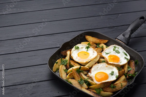 Obraz Breakfast in the pan. Fried potatoes with eggs in a skillet. Food bachelor. Cooked by a man. Hot and fresh. Homemade breakfast on black table. Fried eggs and sweet potato hash in cast iron skillet Fre