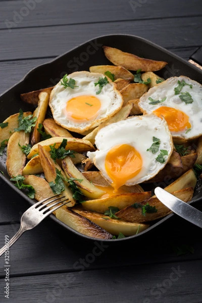 Obraz Breakfast in the pan. Fried potatoes with eggs in a skillet. Food bachelor. Cooked by a man. Hot and fresh. Homemade breakfast on black table. Fried eggs and sweet potato hash in cast iron skillet Fre