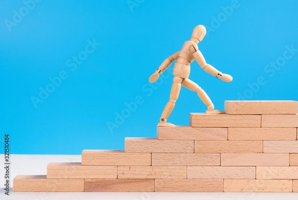 Fototapeta Figure of wooden man climb up the stairs of success or career. Concept of career up, success in life, personal development and progress. Copy space for ad or text. Blue background. Long wooden bricks