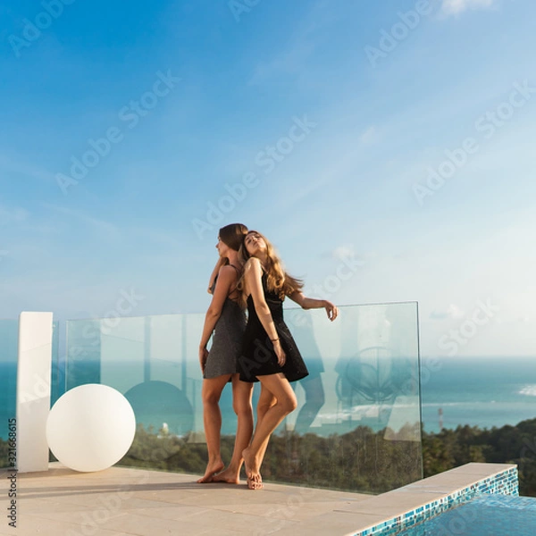 Fototapeta Beautiful girls in an evening dress have fun by the pool with wine and talk about travels and weekends. Discuss March 8th. Leisure and pool parties in a villa by the sea. Thailand, Samui