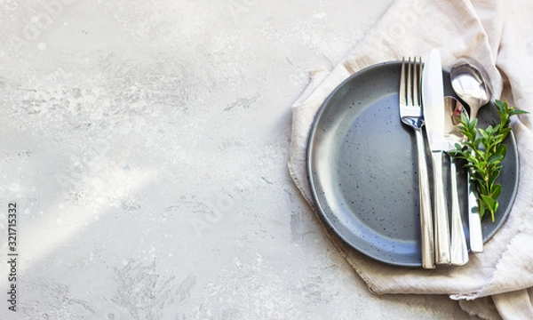 Obraz Elegant table setting with black ceramic plate, cutlery and canvas napkin on grey stone background. Space for text.