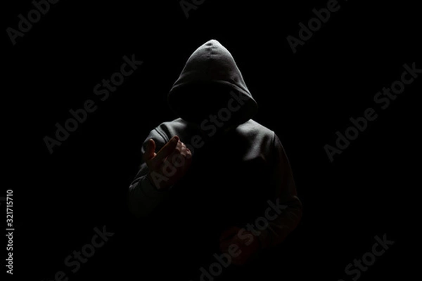 Fototapeta an unknown person in a hood lures into the darkness