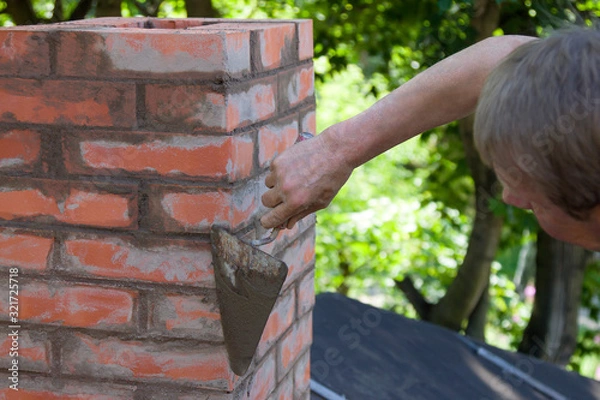 Obraz A man making masonry works, working with a trowel and making a chimney of red bricks