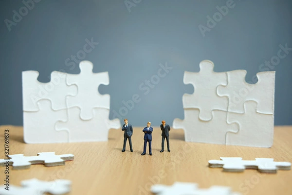 Fototapeta Business strategy conceptual photo - Group of miniature businessman standing on wooden table in front of missing piece puzzle