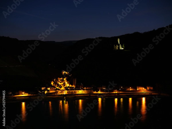 Obraz Night shot of Castle Maus, colorfully illuminated, in front of the Rhine valley and under a starry sky. Below the small city of Wellmich