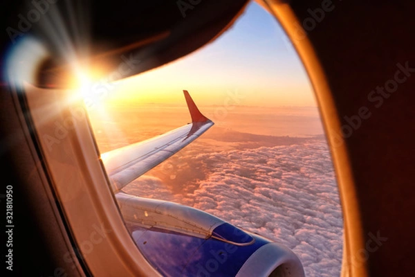Fototapeta plane wing from airplane window seat in flight nature landscape against scenic sunset sky background. Aerial view from aircraft passenger cabin on beautiful red orange sunrise cloudscape and blue sky
