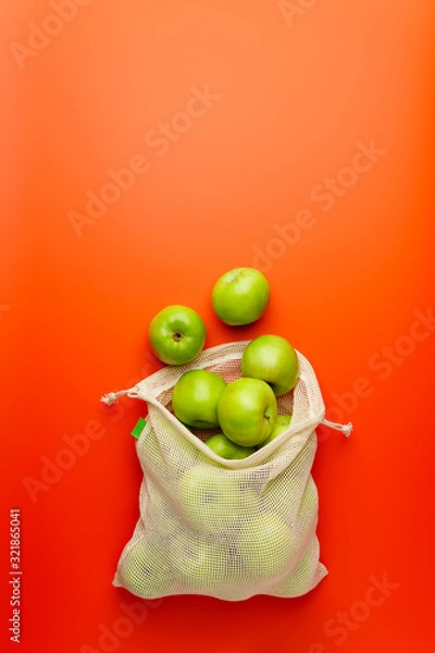 Fototapeta Green apples in a mesh grocery bag on a red background. Flat lay, copy space. Zero waste and no plastic concept.