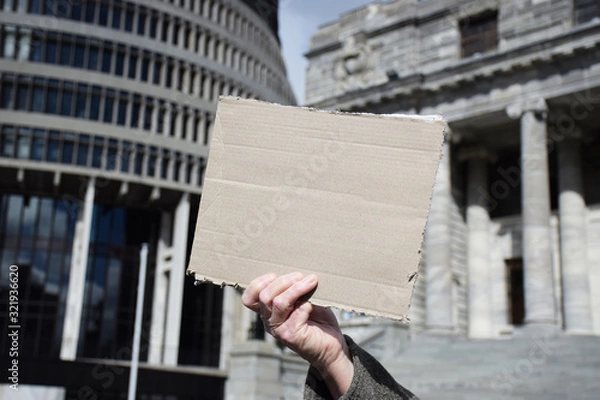 Fototapeta A hand holds up a picket sign outside a parliament building