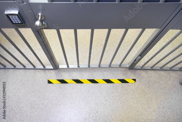 Fototapeta Metal bar security door in the bank with an electronic lock with keypad and steel bobble handle. Do not cross yellow sign on the floor. 