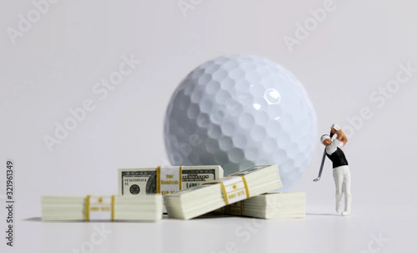 Fototapeta A bunch of $100 bills and a miniature golfer in front of a white golf ball.