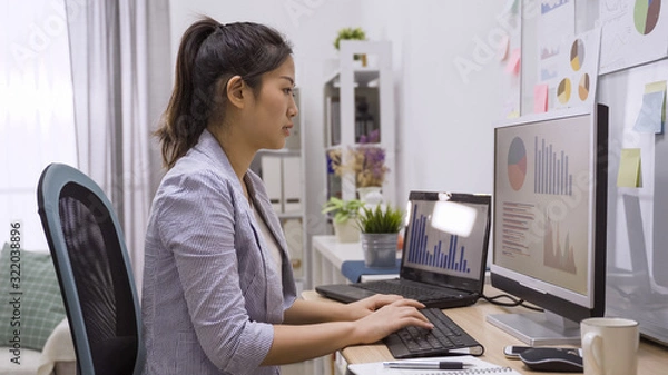 Fototapeta side view image of professional businesswoman in smart casual suit working at modern home office via laptop. young asian female manager using portable computer device while sitting at workplace