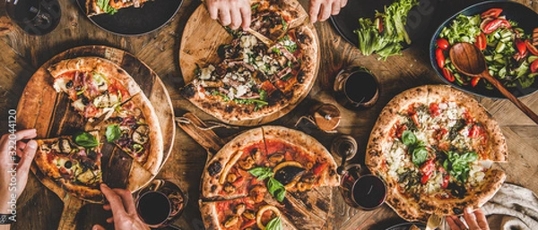 Fototapeta Family or friends having pizza party dinner. Flat-lay of people eating various kinds of Italian pizza and drinking wine over wooden table, top view, wide composition. Fast food lunch concept