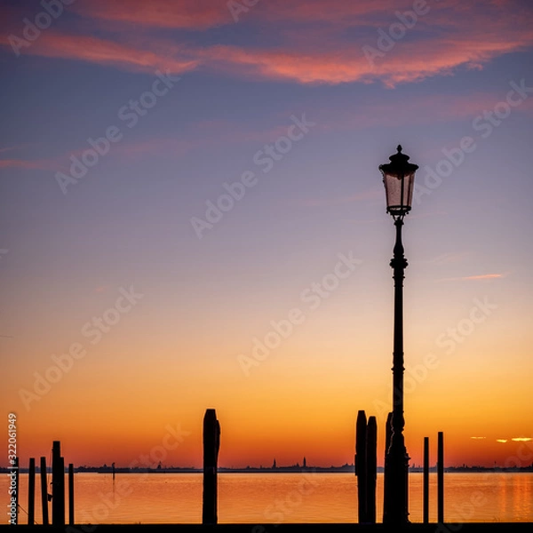Fototapeta Silhouette of a streetlamp at sunset with the island of Venice in the background 