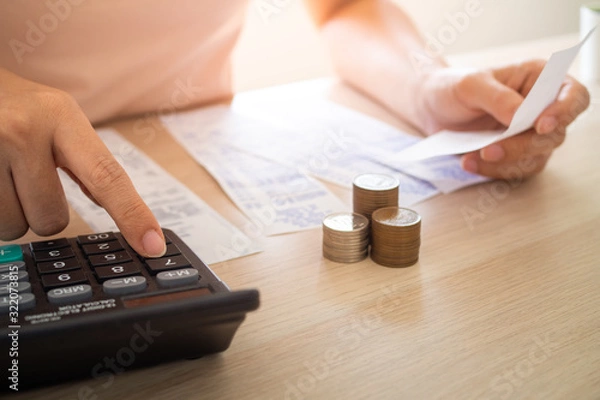 Fototapeta The woman sitting and examining the bill press the calculator to calculate the amount of income, expenses and expenses on the table. Inside the living room at home.