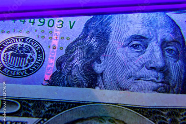 Fototapeta Extreme closeup on dollar banknote under ultraviolet light. Benjamin franklin portrait being inspected. Money falsification concept background.