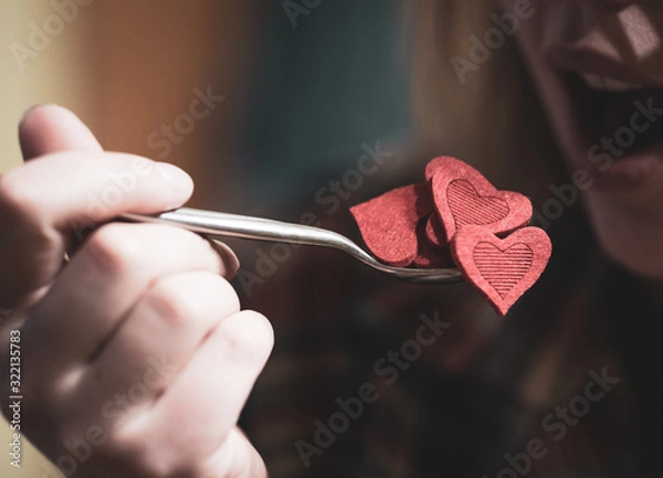 Fototapeta Woman pretending to eat red heart shape figures from the spoon. Selective focus. Valentine's day concept.