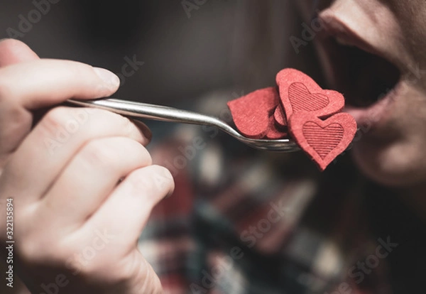 Obraz Woman pretending to eat red heart shape figures from the spoon. Selective focus. Valentine's day concept.
