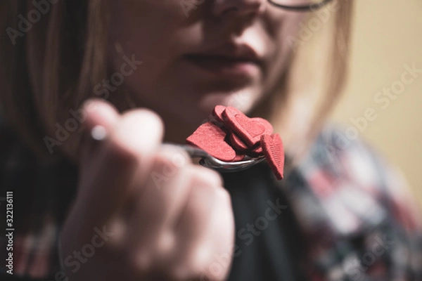 Obraz Woman pretending to eat red heart shape figures from the spoon. Selective focus. Valentine's day concept.