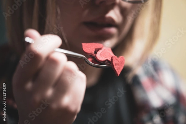 Fototapeta Woman pretending to eat red heart shape figures from the spoon. Selective focus. Valentine's day concept.