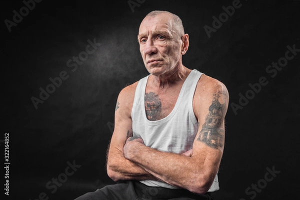 Obraz Portrait of an old man with tattoos in a white T-shirt on a black background
