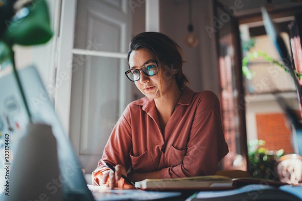 Obraz Pretty young woman an advertising copywriter in eyeglasses working at home using laptop, female graphic designer working in modern studio, Networking Freelancer Businesswoman Designer Entrepreneur