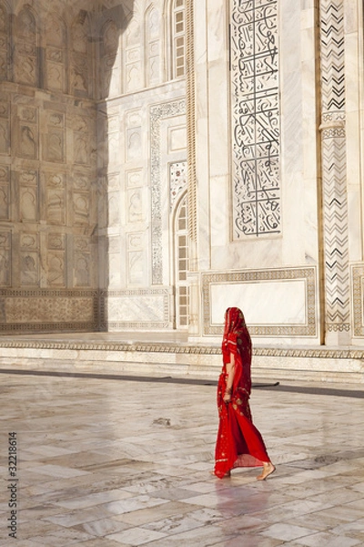 Fototapeta Kobieta w czerwonym sari / sari przechodzi obok Taj Mahal.