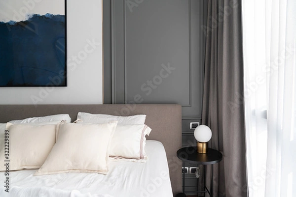 Fototapeta Cozy bedroom corner with modern brown fabric bed headboard and comfortable pillows  setting with gold lamp and modern plug install on gray color classic wall on the background /Interior design 