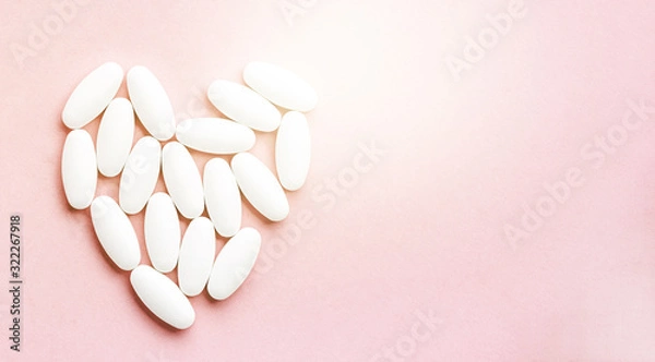 Fototapeta white heart from tablets and pills isolated on pink background with sunlight.