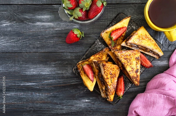 Obraz Sweet french toasts with banana, chocolate, strawberries on a wooden background. Tasty breakfast. Top view