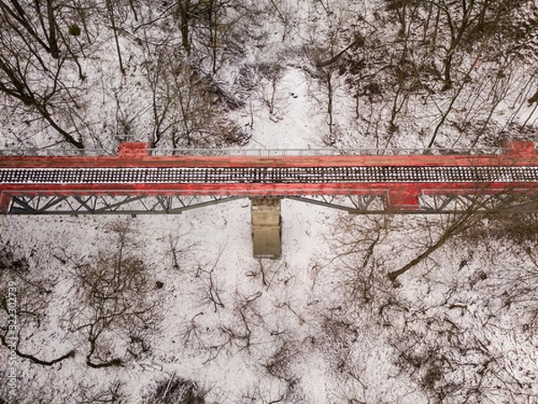 Fototapeta Aerial drone view. Bright red railway bridge among a snowy park.