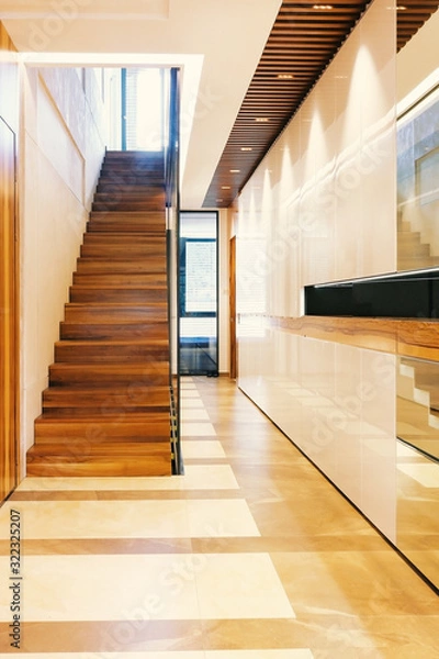 Fototapeta Bright modern hall with glossy surfaces, wooden staircase, ladder ceiling with lights and tiles floor