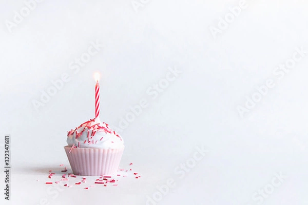 Fototapeta on a white background there is a beautiful cupcake in a pink tin with airy white whipped cream with one hot red and red striped candle i with a beautiful sprinkle of candy
