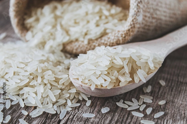 Obraz White rice scattered from a bag on a background of old boards. Jasmine rice for cooking.