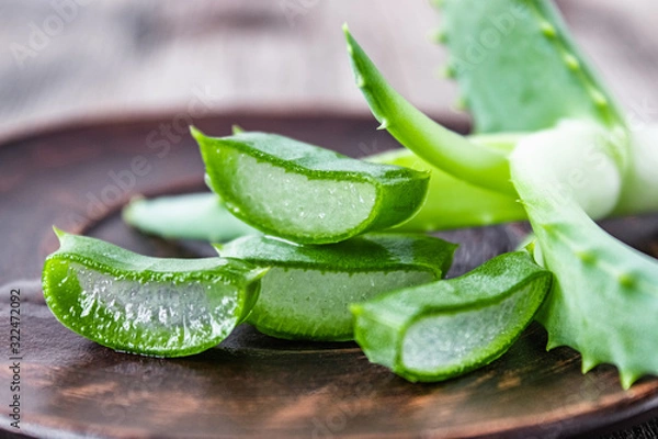Obraz Pieces of aloe vera and fresh leaves lie on a bowl against the background of old boards.