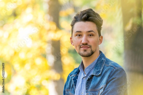 Fototapeta Handsome young man looking at the camera. Portrait of a confident and successful young man with a denim jacket and blue shirt outside. Happy guy smiling